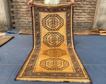 May include: A rectangular runner rug featuring a golden-yellow field with four dark brown octagonal geometric medallions arranged vertically. The border is dark brown with a repeating pattern and small pink accents along the bottom edge.