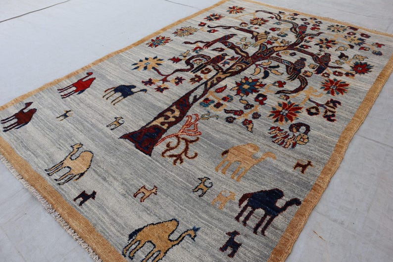 May include: A rectangular area rug with a light gray background and a tan border. The rug features a large central tree with dark brown branches, colorful floral motifs, and various animal figures including camels in red, blue, and tan.
