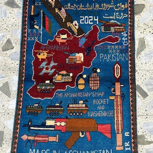 以下が含まれることがあります： 青い背景に赤いアフガニスタンの地図が描かれた長方形のラグ。 ラグには軍用車両、武器、および「2024」や「Made in Afghanistan」を含む複数の言語のテキストが描かれています。