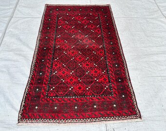May include: A rectangular area rug featuring a deep red and black color palette with a repeating geometric pattern of octagonal motifs. The rug is framed by a wide border with intricate linear designs and includes short white fringe at both ends.
