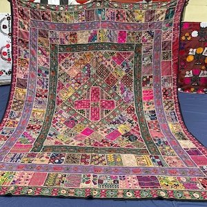 May include: A large rectangular textile wall hanging featuring a vibrant patchwork of multi-colored fabric squares. The design includes intricate embroidery, small mirrors, and a central cross motif surrounded by various geometric patterns.