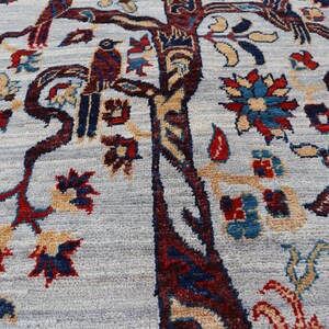 May include: A light blue area rug featuring a detailed woven pattern of a large central tree with dark red and brown bark. The design includes stylized birds perched on branches, surrounded by intricate floral motifs in red, blue, and tan.