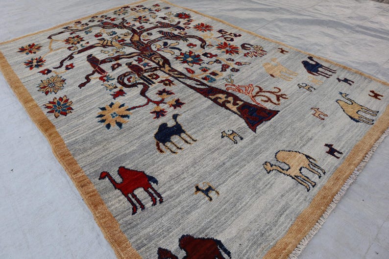 May include: A rectangular area rug with a light gray field and a tan border. The rug features a large central tree motif with dark brown branches, colorful floral blossoms, and various animal figures including camels in red, blue, and tan.