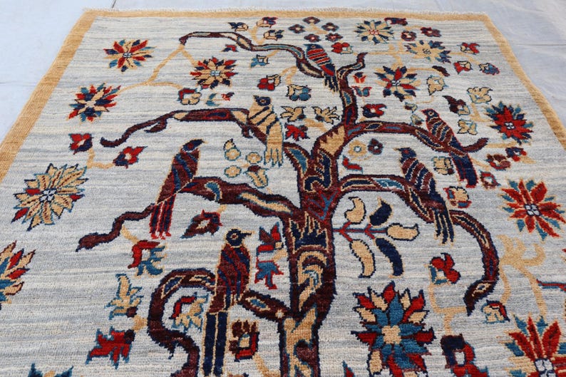 May include: A rectangular area rug featuring a light gray background with a central dark brown tree motif. The tree branches are adorned with various birds in shades of red, blue, and brown, interspersed with colorful floral patterns in red and blue.