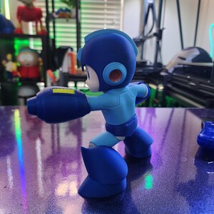 Puede incluir: Una figura de acci&oacute;n de pl&aacute;stico azul y amarillo de un personaje robot con un gran ca&ntilde;&oacute;n de brazo. La figura est&aacute; en una postura de lucha con una pierna hacia adelante y la otra hacia atr&aacute;s.