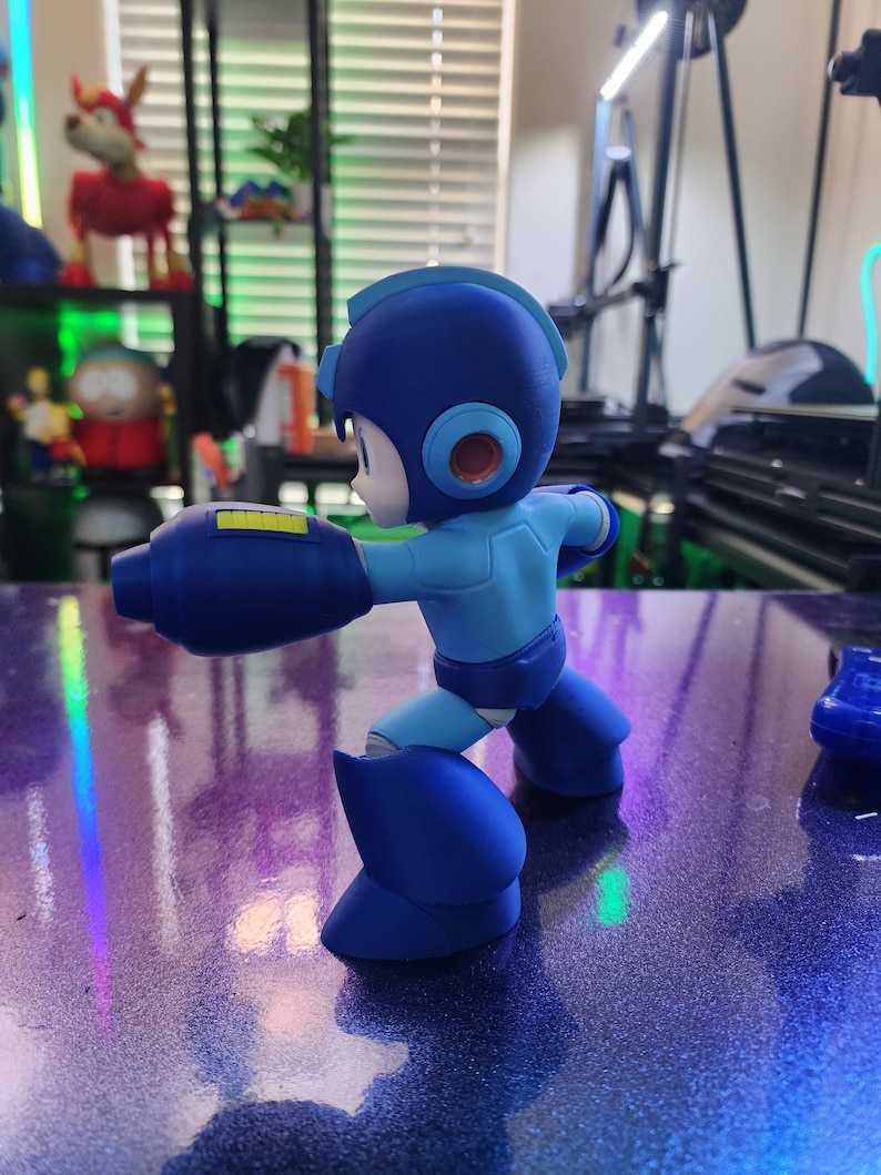 Puede incluir: Una figura de acci&oacute;n de pl&aacute;stico azul y amarillo de un personaje robot con un gran ca&ntilde;&oacute;n de brazo. La figura est&aacute; en una postura de lucha con una pierna hacia adelante y la otra hacia atr&aacute;s.