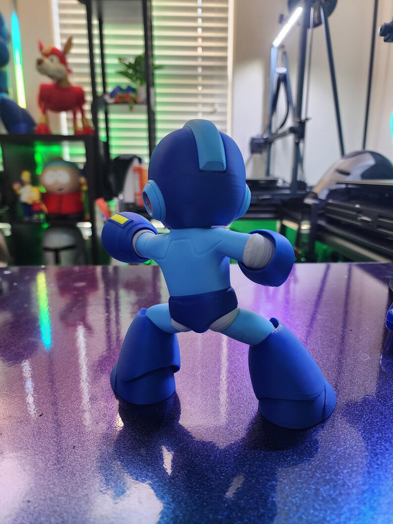 Puede incluir: Una figura de robot azul y amarillo con un casco y un cuerpo azul. El robot est&aacute; de pie con las piernas separadas y los brazos levantados.