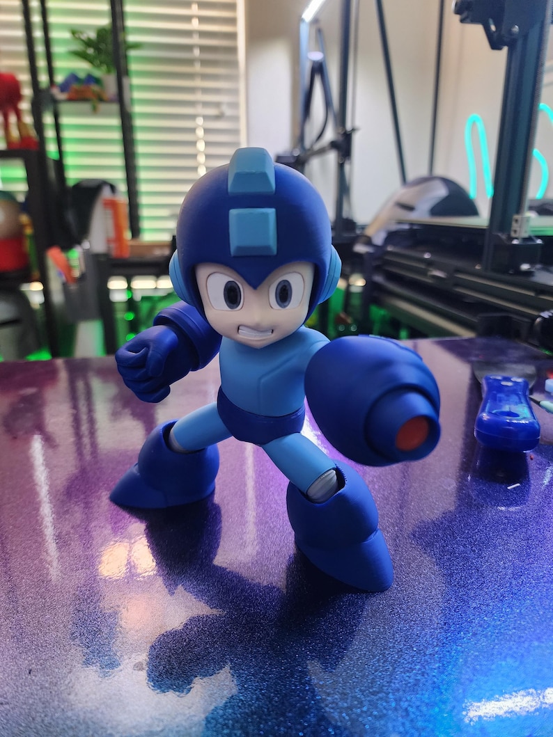 Puede incluir: Una figura de acci&oacute;n de pl&aacute;stico azul y azul claro de un robot con un gran ca&ntilde;&oacute;n de brazo. El robot tiene un casco azul con una visera azul claro y una cara azul claro con una expresi&oacute;n decidida.