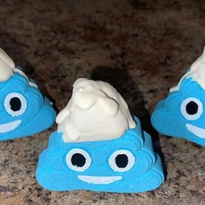 Puede incluir: Tres bombas de baño azules con forma de emoji de caca sonriente con glaseado blanco en la parte superior.