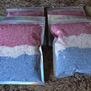 Puede incluir: Cinco bolsas de plástico transparentes llenas de sales de baño de colores. Las sales están en capas de color rosa, blanco y azul.