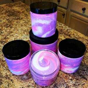 May include: Four jars of whipped body butter in various shades of pink and purple. The jars have black lids and are arranged in a pyramid shape.