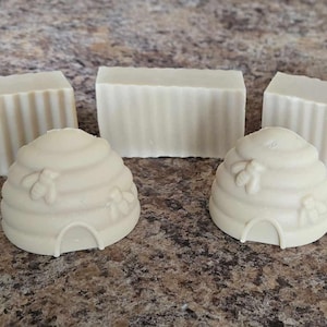 May include: Three bars of white soap with a striped pattern and two white soap beehive sculptures.