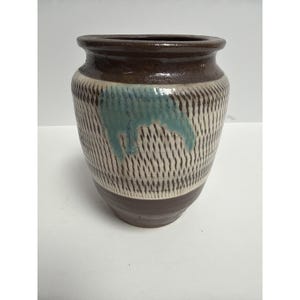 Puede incluir: Un jarrón de cerámica marrón y blanco con un patrón de rayas verticales texturizadas. El jarrón tiene un borde y una base de color marrón oscuro, con una salpicadura de esmalte turquesa. Un artículo de decoración del hogar.