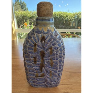 Könnte beinhalten: Eine handgefertigte Keramikflasche mit einem strukturierten blau-braunen Design. Die Flasche hat einen Korken und eine einzigartige, organische Form. Die Flasche ist etwa 20 cm hoch, perfekt zum Ausstellen oder Aufbewahren von Flüssigkeiten.