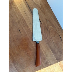 May include: A vintage cake server. It has a stainless steel blade and a brown handle. The blade is rectangular with a slightly rounded tip. The handle is a dark brown colour and appears to be made of a hard plastic or resin material.