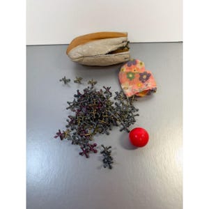 May include: A vintage jacks game set with a leather pouch, a floral print fabric pouch, a red rubber ball, and a pile of metal jacks. The jacks are in various colors, including silver, bronze, and purple.