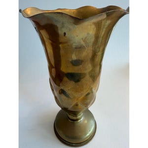 May include: A polished brass vase featuring a wide, scalloped, and flared rim that tapers down to a narrow neck, expanding into a rounded, textured body with embossed diamond-shaped patterns, supported by a circular, smooth pedestal base.