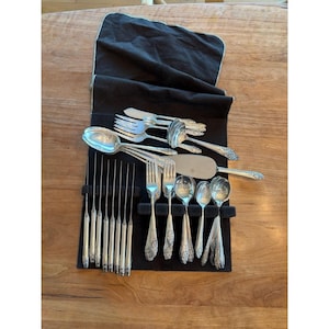 Könnte beinhalten: Eine Sammlung von Ziersilber, darunter Gabeln, Löffel, Messer und Servierutensilien, präsentiert in einem schwarzen, mit Filz gefütterten Roll-Etui. Das Silberbesteck weist detaillierte Blumenmuster und eine glänzende Oberfläche auf.