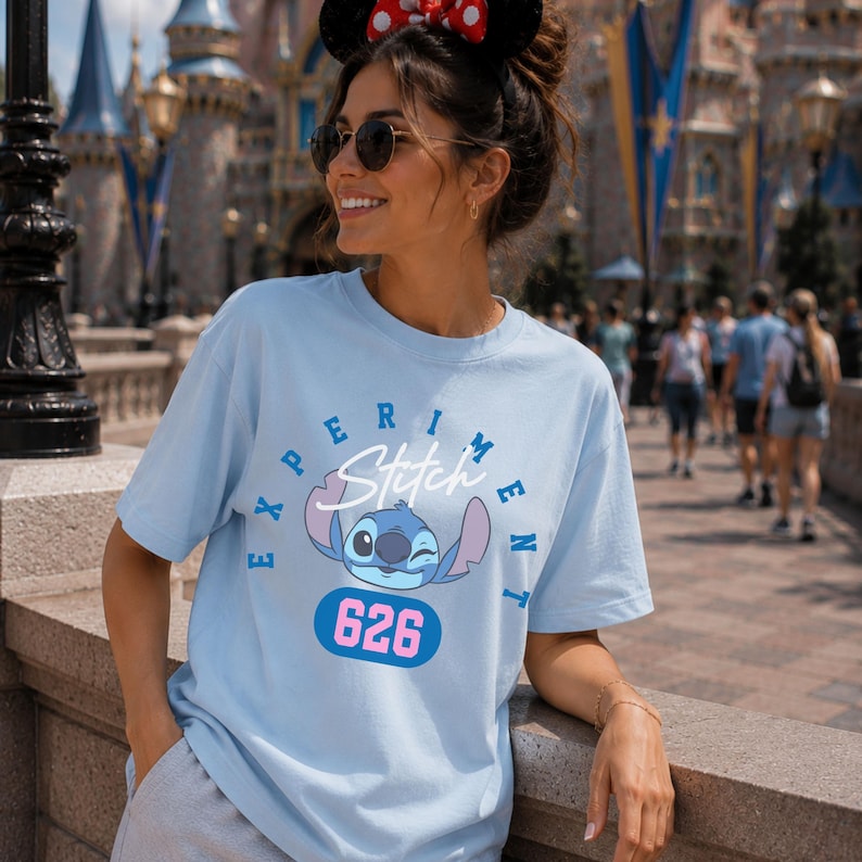 May include: Light blue t-shirt featuring a graphic of Stitch from Lilo & Stitch, with the text "Experiment" and "626". The shirt has a crew neck and short sleeves. The design is in shades of blue, pink, and white.