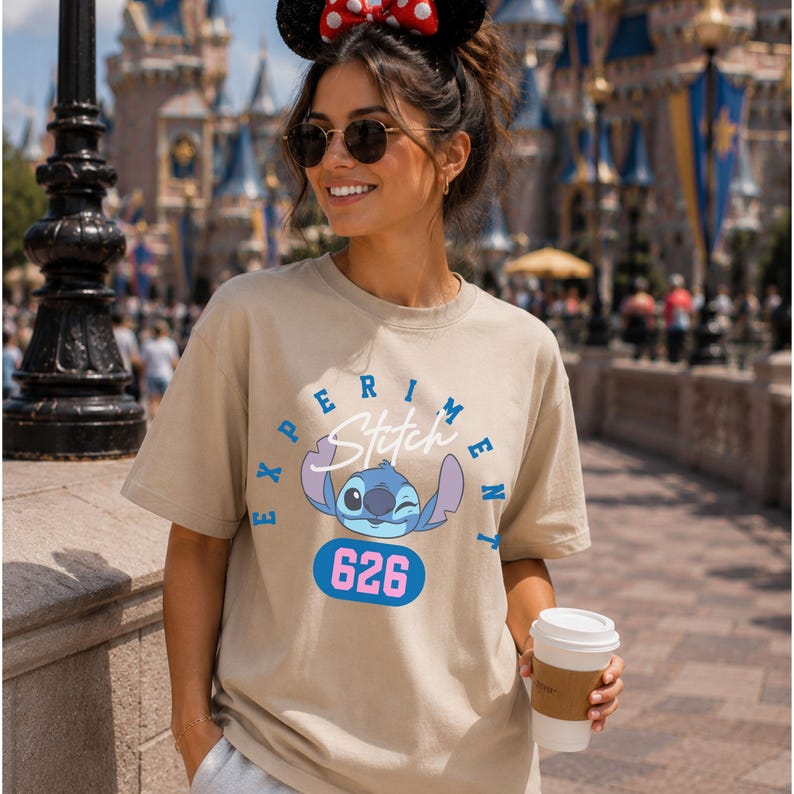 May include: A beige t-shirt featuring a graphic of the character Stitch from the movie Lilo & Stitch. The design includes the word "Experiment" and the number "626". The shirt is short-sleeved and has a crew neck.