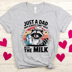 May include: A gray t-shirt with a retro-style design featuring a raccoon wearing a chef's hat and holding a carton of milk. The text on the shirt reads 