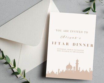 May include: A white invitation card with brown text that reads "You are invited to Aliyah's Iftar Dinner Saturday, March Fifteenth Five o'clock in the evening". The card features a silhouette of a mosque and other buildings in a light brown color.