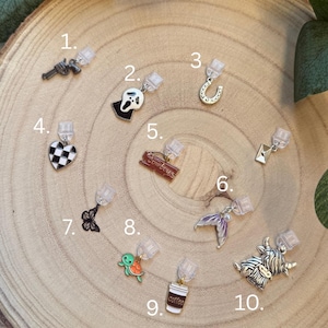 May include: A selection of ten stud earrings with diverse designs. These include a gun, a ghost, a horseshoe, a checkered heart, a sign that says "Cowboys", a mermaid tail, a butterfly, a turtle, a coffee cup, and a Highland cow.