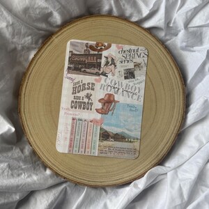 May include: A rectangular collage with cowboy-themed illustrations, including a hat and boots, and text that reads "Save a Horse Ride a Cowboy." The collage is on a wooden slice, set against a white fabric background.