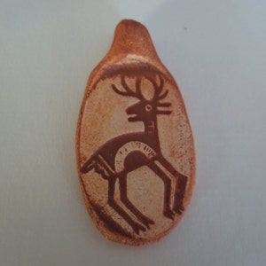 May include: A ceramic pendant in the shape of a deer with a brown and white glaze. The deer is stylized with a simple design and is facing to the right.