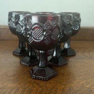 May include: A set of five deep red glass goblets featuring a textured hobnail pattern on the bowl. Each goblet has a thick stem and a hexagonal base, crafted from pressed glass with a consistent dark crimson hue throughout the entire collection.