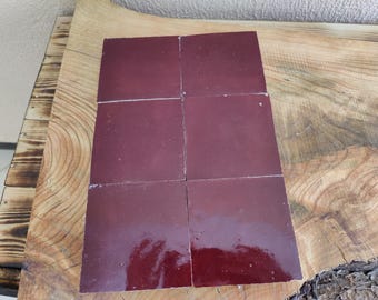 May include: Four square burgundy tiles arranged in a grid pattern. The tiles are smooth and glossy.