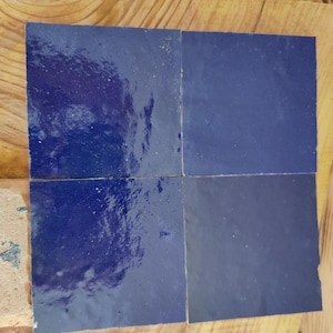 Könnte beinhalten: Vier quadratische Keramikfliesen in einem tiefen Blau. Die Fliesen sind in einem 2x2 Raster angeordnet.
