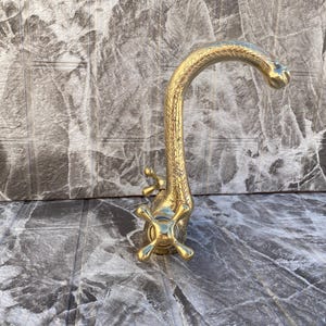 Può includere: Un rubinetto dorato con un becco curvo decorativo e maniglie a forma di croce.