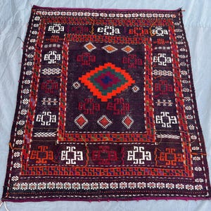 May include: A rectangular, hand-woven rug with a dark purple background and intricate geometric patterns. The central design features a diamond shape in red, orange, green, and blue. The border includes white, red, and orange accents.