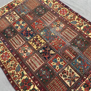 May include: A rectangular area rug featuring a grid of square panels, each containing distinct floral and geometric motifs in shades of deep red, navy blue, forest green, and cream. The border displays a repeating pattern of stylised plants.