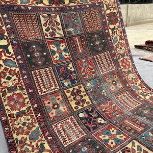 May include: A rectangular area rug featuring a grid of individual panels, each containing distinct floral and geometric motifs in shades of deep red, navy blue, forest green, and cream. The wide border displays a repeating pattern of stylised flowers.