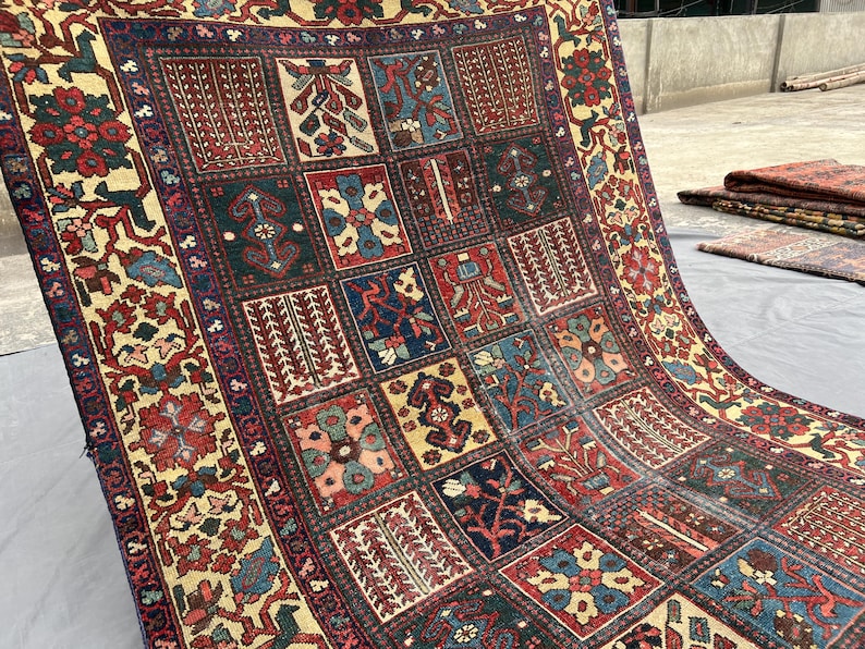 May include: A rectangular area rug featuring a grid of individual panels, each containing distinct floral and geometric motifs in shades of deep red, navy blue, forest green, and cream. The wide border displays a repeating pattern of stylised flowers.