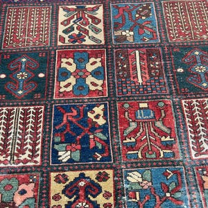 May include: A rectangular area rug featuring a grid of square panels, each containing distinct geometric and floral motifs in shades of deep red, navy blue, cream, and teal. The design is composed of repeating patterns within bordered sections.