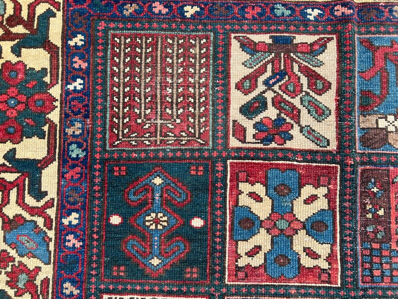 May include: A woven rug featuring a grid of rectangular panels with intricate geometric and floral patterns in shades of deep red, navy blue, and cream. The border displays a repeating floral motif on a cream background with blue accents.