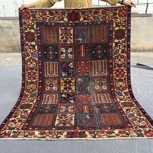 May include: A rectangular area rug featuring a grid of various geometric and floral patterns in shades of red, blue, cream, and dark brown. The rug has a wide decorative border with floral motifs and a short white fringe along the bottom edge.