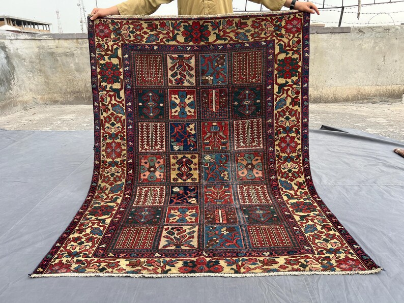 May include: A rectangular area rug featuring a grid of various geometric and floral patterns in shades of red, blue, cream, and dark brown. The rug has a wide decorative border with floral motifs and a short white fringe along the bottom edge.