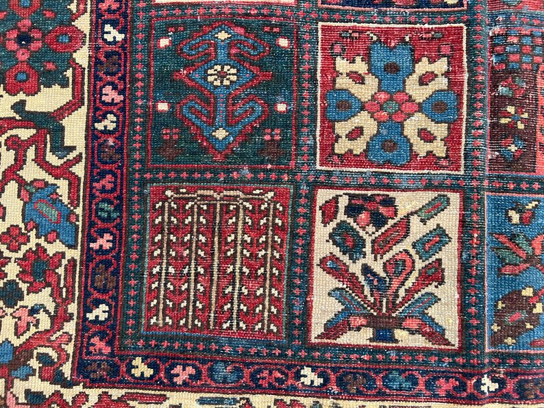 May include: A woven rug featuring a grid pattern of square panels. Each panel contains distinct geometric and floral motifs in shades of deep red, navy blue, cream, and teal. The border displays intricate repeating patterns in matching colours.