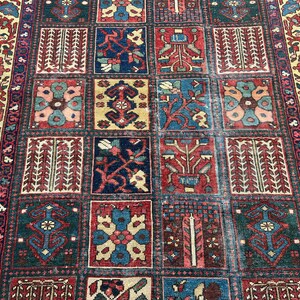 May include: A rectangular area rug featuring a grid of square panels, each containing distinct floral and geometric motifs in shades of deep red, navy blue, cream, and teal. The border displays a repeating pattern of stylised flowers and vines.