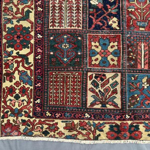 May include: A rectangular area rug featuring a grid of square panels, each containing distinct floral and geometric motifs in shades of deep red, navy blue, cream, and teal. The border displays a repeating pattern of flowers and vines.