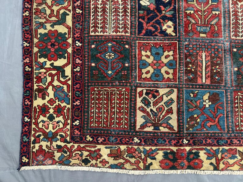May include: A rectangular area rug featuring a grid of square panels, each containing distinct floral and geometric motifs in shades of deep red, navy blue, cream, and teal. The border displays a repeating pattern of flowers and vines.