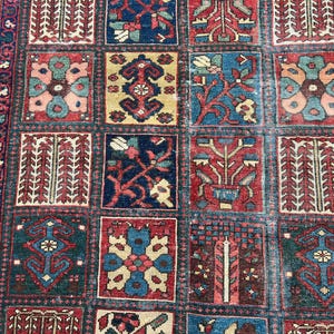 May include: A rectangular area rug featuring a grid of square panels, each containing distinct floral and geometric motifs in shades of deep red, navy blue, cream, and teal. The border displays a repeating pattern of stylised blossoms and vines.