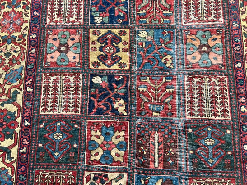 May include: A rectangular area rug featuring a grid of square panels, each containing distinct floral and geometric motifs in shades of deep red, navy blue, cream, and teal. The border displays a repeating pattern of stylised blossoms and vines.