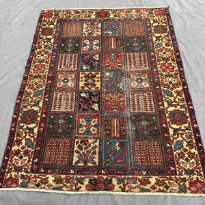 May include: A rectangular area rug featuring a grid of various floral and geometric motifs in shades of deep red, navy blue, forest green, and cream. The rug has a wide decorative border with repeating botanical patterns and short white fringe.