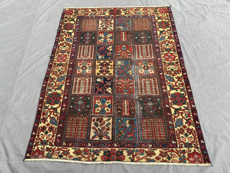 May include: A rectangular area rug featuring a grid of various floral and geometric motifs in shades of deep red, navy blue, forest green, and cream. The rug has a wide decorative border with repeating botanical patterns and short white fringe.