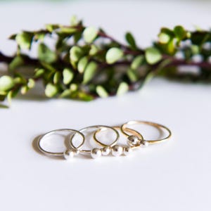 May include: Four simple silver rings with a single bead on each ring. The rings are stacked on top of each other, with the gold ring on top.
